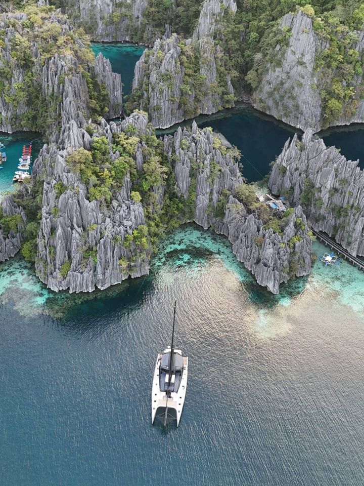 A catamaran anchored below limestone cliffs, seen from the air